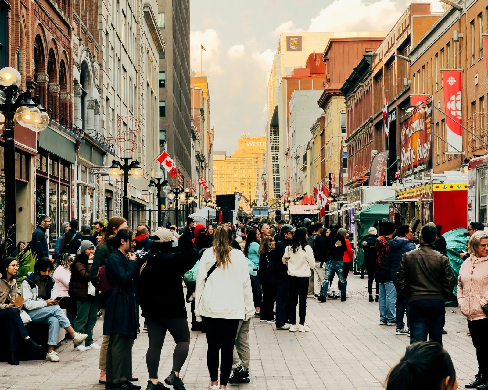 Une rue piétonne animée au centre-ville d’Ottawa, avec des kiosques de nourriture, des drapeaux canadiens et des immeubles de brique anciens.